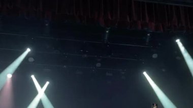 Parlak sahne ışıkları karanlık bir tiyatroda parlıyor, ışık saçıyor ve performanslar için çekici bir ortam yaratıyor.