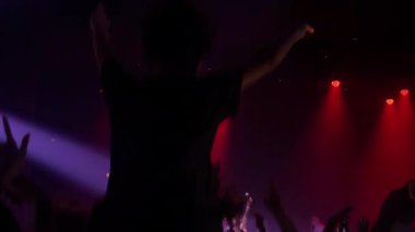 Kalabalık bir konserde canlı müzik dinliyor. Renkli ışıklar sahneyi aydınlatıyor ve kutlamalar yapılıyor.