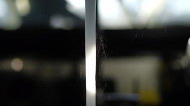 Mutfaktaki modern metal musluktan koyu bulanık arka planı olan su akışının yakın plan görüntüsü