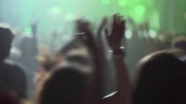 Yeşil sahne ışıkları ve bulanık arkaplan ile konserde seyirciler ellerini havaya kaldırıyor