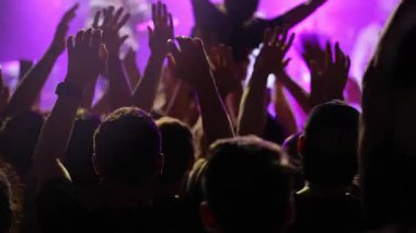 Canlı konserdeki enerjik kalabalık, kutlama için ellerini kaldırmış, renkli sahne ışıkları ile aydınlatılmış, canlı bir atmosfer yaratıyor.