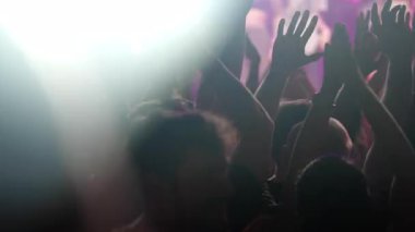 Coşkulu kalabalık, elleri havada, renkli ışıklar ve heyecanla çevrili, canlı bir müzik konserinin atmosferine dalmış.