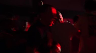 Canlı bir kalabalığın partide dans edişinin dinamik sahnesi, renkli ışıklarla aydınlatılmış, enerjik ve neşeli bir ortam yaratıyor.