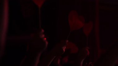 Seyirciler canlı bir konserde kırmızı kalp işaretleri kaldırıyor. Işıkları yakıp enerjik bir atmosfer yaratıyorlar.