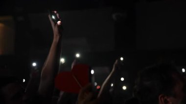 Elleri havada, akıllı telefonları olan, parlak ışıklarla aydınlatılan, enerjik bir atmosfer yaratan bir grup konsere gidenler.