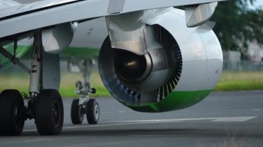 Uçak motoru ve iniş takımlarının yakın çekim görüntüsü, türbin tasarımı ve yeşil aksanları vurgulanıyor, havacılık teknolojisi vurgulanıyor