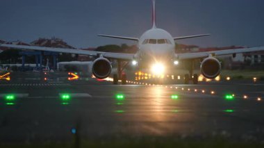Uçak gece kalkış pistinde, aydınlık ışıklar ve karanlık gökyüzü ile çevrili, dramatik bir havacılık sahnesi yaratıyor.