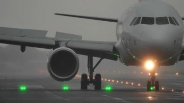 Uçak pistte taksicilik yapıyor, etrafı sislerle çevrili, yeşil ışıklar yolu gösteriyor, dramatik bir havacılık sahnesi yaratıyor