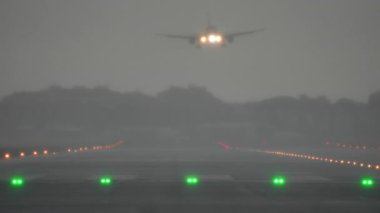 Şiddetli yağmur sırasında sislerle çevrili yeşil ve kırmızı ışıklarla uçak piste yaklaşıyor.