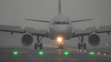 Pistte sisli ve yağmurlu koşullarda taksicilik yapan uçaklar, önlerindeki yolu aydınlatan yeşil ışıklarla havacılık operasyonlarını gösteriyor.
