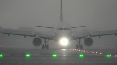 Uçak yağmurda sisli koşullarda piste yaklaşıyor.