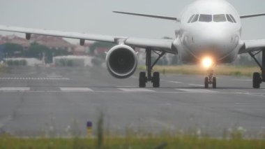 Uçak pistte taksicilik yapıyor, bulanık havalimanı arka planı ve bulutlu gökyüzü, alçak açılı çekim