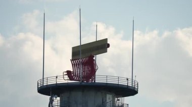 İletişim kulesinde radar ekipmanları ve antenler var, kabarık bulutların zemininde yükseliyor, modern teknoloji ve mühendislik sergileniyor.