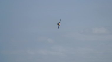 Askeri jet uçağı yemyeşil tepelerin ve yerleşim alanlarının üzerinde uçuyor.