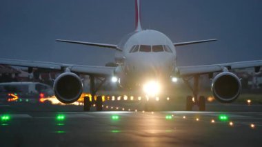 Pistte taksicilik yapan ticari uçakların ön görüntüsü düşük ışık koşullarında parlak farlarla