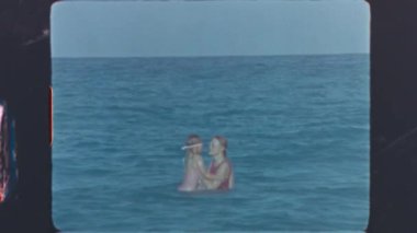 Anne, klasik 8mm filmle kızını oynatıp denize atıyor.