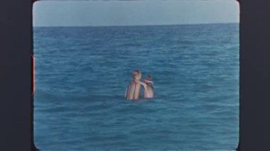 Anne ve kızı mavi denizde birlikte yüzmenin keyfini çıkarıyorlar.