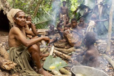 Baka kabilesinden bir pigme kadın Kamerun yağmur ormanlarında çocuklarla yemek yiyor. Bir orman topluluğundaki günlük hayata bir bakış.