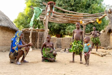 Kamerun Dupa kabilesinde köy hayatı. Bir kadın yaprak gibi bir etek yapan bir kıza gülümserken, bir oğlan ve bir bebek yakınlarda dikiliyor. Topluluk, gelenek ve neşe bir çerçevede