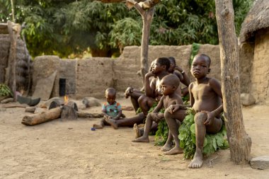 Dupa kabilesi üyeleri Kamerun 'daki bir çamur barakasının dışında dinleniyor, sıcak akşam ışığında geleneksel yaprak kıyafetleri giyiyorlar.