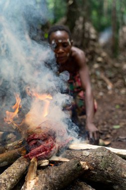 Baka adam ormanda açık ateşte taze çalı eti pişiriyor. Geleneksel aşçılık metodu kabile orman yaşamına dayanıyor..