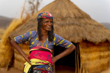 Geleneksel kıyafetli gülümseyen Mbororo kadın Kamerun 'da sazdan bir kulübede duruyor, otantik Afrika kabilesinin yaşamını yakalıyor..