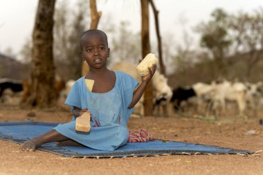 Genç Mbororo 'lu çocuk bir paspasın üzerinde oturur ve kırsal Kamerun' da çocukluğun basitliğini ve orijinalliğini gösterir..