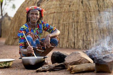 Mbororo 'lu kadın kulübesinin önündeki açık ateşte yemek pişiriyor, günlük yaşamını ve kırsal Kamerun geleneklerini yakalıyor..