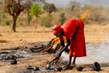 Çömlek atımının son aşamasında Dowayo kabilesinin baş karısı, Kamerun kırsalındaki dumandan bitmiş kil damarlarını kaldırıyor..