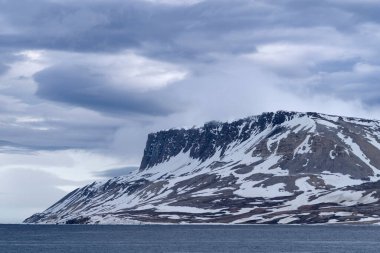 Svalbard 'ın karla kaplı kayalıkları Kuzey Denizi' nin üzerinde yükseliyor. Ham kuzey güzelliğinin dramatik bir manzarası ve kutup doğasının sertliği..