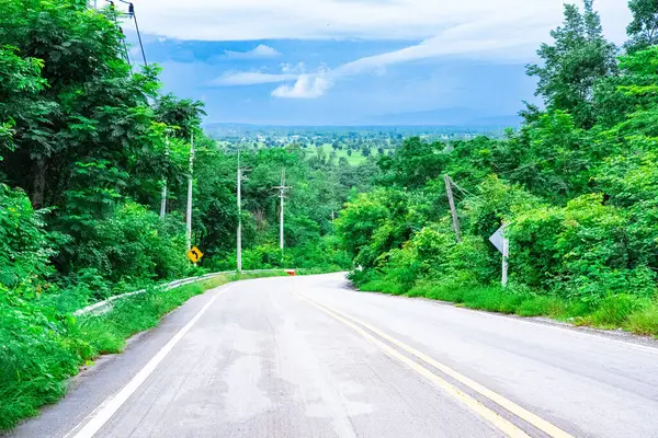 Yolun her iki tarafında da güzel yeşil ağaçlarla dağdan inen manzarası. Mavi bir gökyüzü var. Atmosfer ziyaret etmeye değer. Bu yol Tayland 'da.
