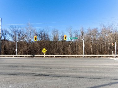 Görüntü, 11. Otoyol 'da trafik ışıkları, yön işareti ve olası bir dönüş olduğunu gösteren sarı bir işaret gösteren bir kavşak yakalıyor. Sahne yapraksız ağaçlar ve açık mavi bir gökyüzü üzerine kurulmuştur.