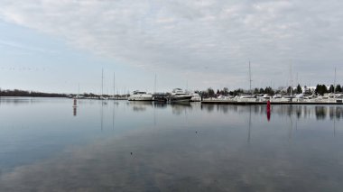 Toronto Kanada 'daki huzurlu liman sahnesinde demirlemiş tekneler, sakin su yansımaları ve CN Kulesi' nin de dahil olduğu uzak bir gökyüzü manzarası görülüyor.