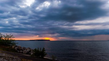 Bulutlu bir gökyüzü ile okyanusun üzerinde güzel bir gün batımı. Gökyüzü karanlık ve su sakin.