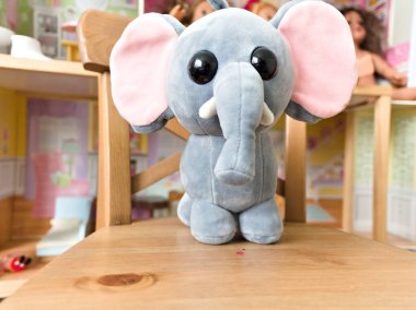 Doldurulmuş bir fil ahşap bir sandalyede oturuyor. Fil pembe bir burun takıyor ve pembe bir kulağı var.