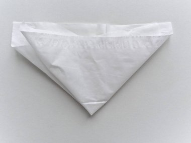 Beyaz bir kağıt üçgen şeklinde katlanır. Kağıt beyaz ve üzerinde bir desen var.