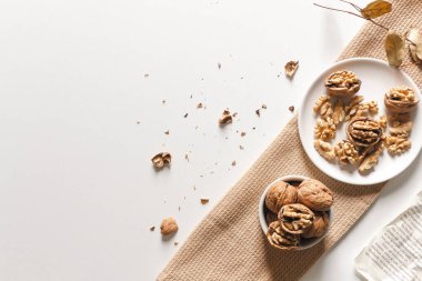 Sıcak sonbahar estetiği konsepti. Ceviz, ceviz kabuğu ve beyaz tabaklarda kuru ceviz çekirdekleri ve bej kumaş.. 