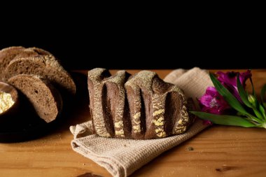 Tam ve dilimlenmiş kahverengi ekmek ahşap masada. Çiçeklerle süslenmiş. Karanlık kompozisyon. Fırın kavramı. 