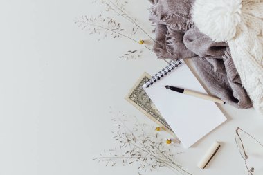 Beyaz arka planda kadın kış aksesuarları. Ilık beyaz örgü şapka, maske, not defteri ve gri eşarp. Düz yatış, üst görünüm. 