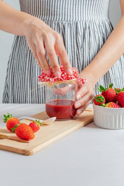 Bir kavanoz çilek reçeli tutan genç bir kadın..