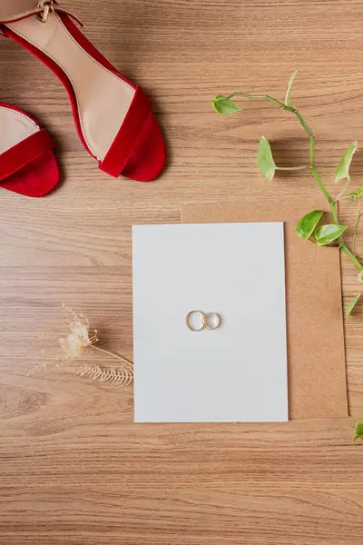 Elements of wedding decor. Wedding rings, wedding green plants, red high heels, and invitation. Indoors, close-up. Wedding preparation concept.