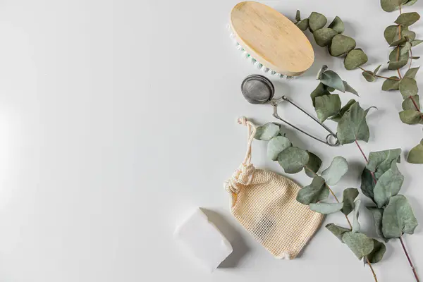 Beige eco style feminine household supplies: cleaning brush, cotton bag, tea strainer, coconut soap and eucalyptus leaves on white background. Flat lay, top view. Eco friendly minimalist concept.