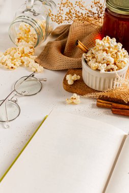 Mutfak gereçlerinde patlamış mısır ve tarçın çubukları, gözlük ve kitapla rahat bir kompozisyon. Sonbahar, kış yemekleri konsepti.