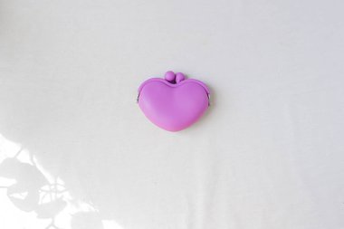 beyaz arka planda mor kalp şekilli bozuk para cüzdanı, biraz yaprak gölgesi. 