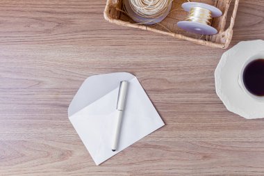 Tahta masadaki zarf. Bir fincan kahve, saman sepeti ve beyaz zarflı ofis masası çalışma alanı 