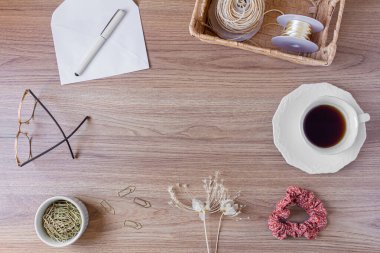 Tahta masadaki zarf. Ofis masası çalışma alanı, yabani çiçekler, bir fincan kahve, saç tokası ve kırtasiye malzemeleri. Düz yerde, üst tarafta. Samimi kompozisyon. Romantik harf kavramı. 