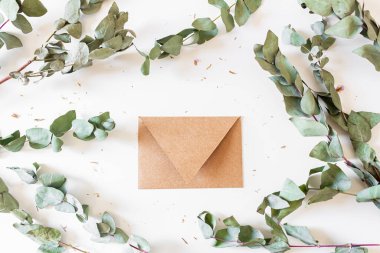 Beyaz zemin üzerinde okaliptüs yaprakları ve dallardan yapılmış yuvarlak çerçeve ve el işi zarfı. 