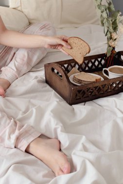 Kahvaltıda ekmek yiyen bir kadın. Yatakta, koyu ahşap bir tepside. 