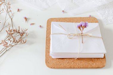 Bej rengi düğün davetiyeleri kompozisyonu. Beyaz zarflar, kurumuş çiçekler, dantel tekstil, beyaz arka planda sisal ip.. 