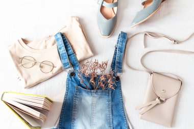 Beyaz çarşaf üzerinde kot tulumları olan kadınsı bahar ve yaz moda kompozisyonu. Düz yerde, üst tarafta. Klasik kıyafet kolajı. Kadın moda blogu ve sosyal medya kavramı.